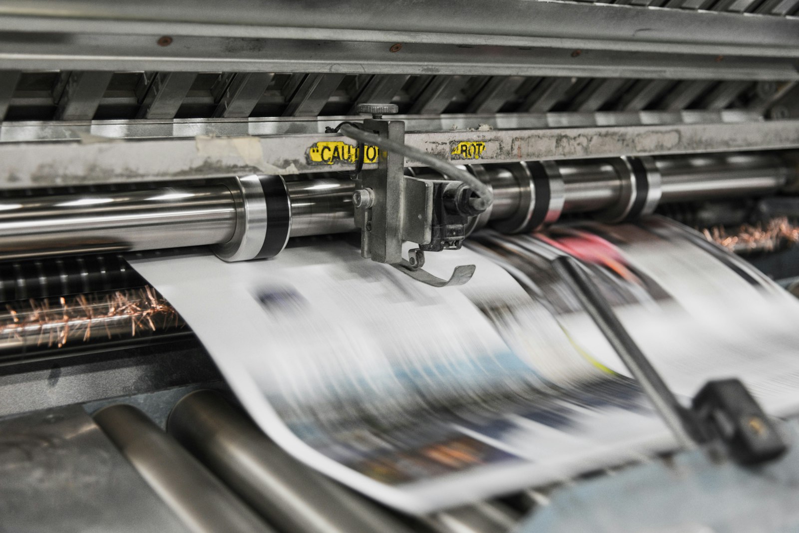 A close-up of a printing press feeding colorful printed pages through metal rollers